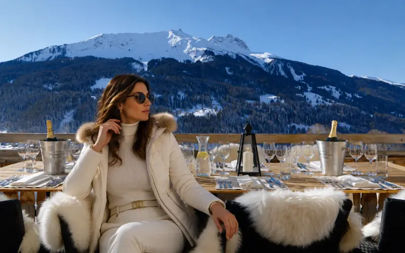 A high-class ski escort companion on an alpine terrace at a luxury European ski resort with Top Companions