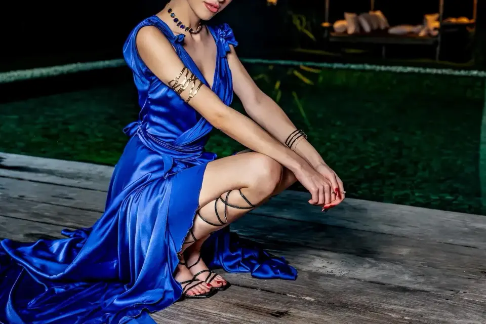 Escorts Amsterdam Airport: elegant escort in a flowing blue satin gown by the pool at night
