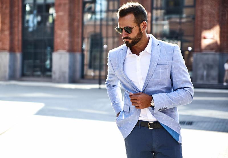 Elegant man in a smart outfit wearing a light blazer, sunglasses, watch and belt, representing refined style for a first escort date.